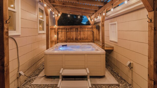 Un jacuzzi en un espacio exterior de madera con una terraza de madera y una pérgola superior.