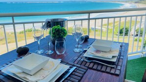 A dining table set with plates, glasses, and cutlery, overlooking a beach and ocean view.