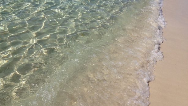 Ein Strand mit klarem, flachem Wasser und sandigem Ufer.