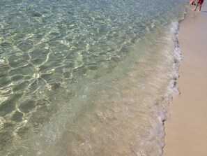 A beach with clear shallow water and a sandy shore.