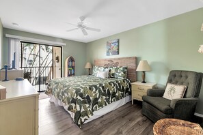 Relax in this serene space with a large bed, armchair, and side table, offering a peaceful view of palm trees.