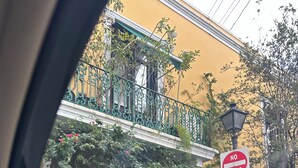 Un edificio amarillo con balcón, un cartel de 'NO ENTRANCE' y plantas en macetas.