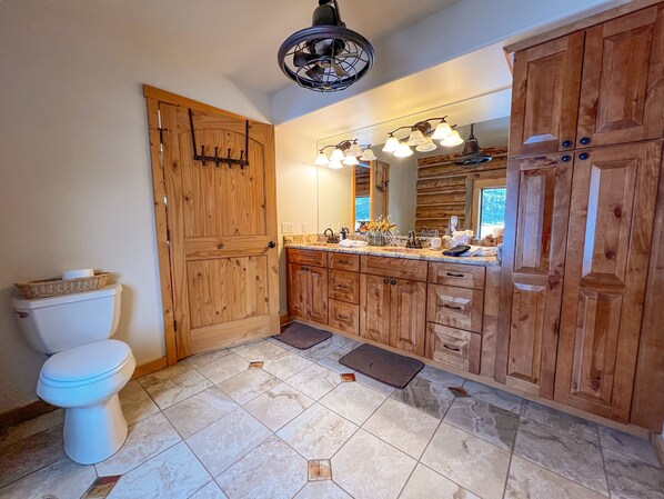 A bathroom with wooden cabinetry, a white toilet, a marble-tiled floor, and a ceiling fan.