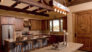 Une cuisine avec des meubles de rangement en bois, un îlot central doté de tabourets, un luminaire suspendu et une porte en bois.