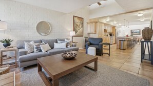 A modern living room with a grey sofa, a wooden coffee table, and a kitchen area in the background.