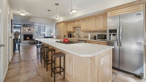 A modern kitchen with a large island, stainless steel appliances, wooden cabinets, and pendant lighting.