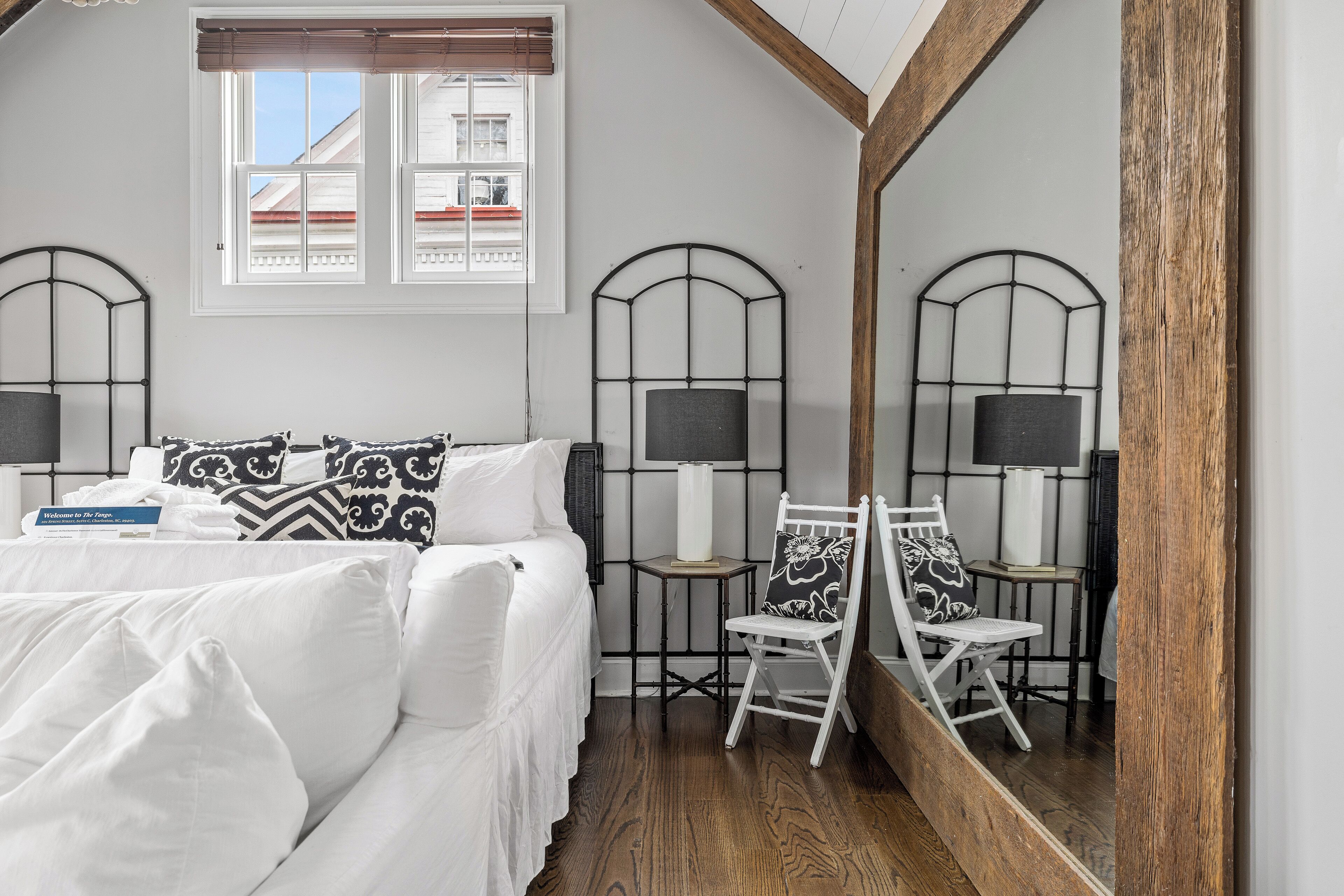 Une chambre à coucher avec un lit, deux chaises, un miroir et une fenêtre.