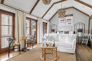 A cozy living room with a white sofa, a round wooden coffee table, and a dining area with a small table and chairs. - Honeymoon Paradise | The Tango (Charleston)