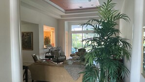 Een ruime woonkamer met een grote bank, een salontafel en een potplant. Er is een raam dat natuurlijk licht en uitzicht op de omgeving biedt.