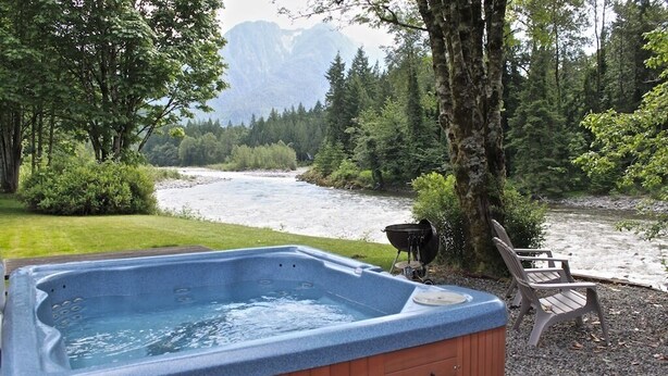 Un bain à remous situé dans une zone boisée, avec une rivière et des montagnes en arrière-plan.