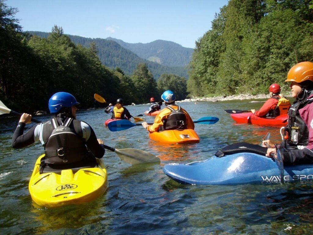Un groupe de personnes pratiquant le kayak sur une rivière, entourée de montagnes boisées.