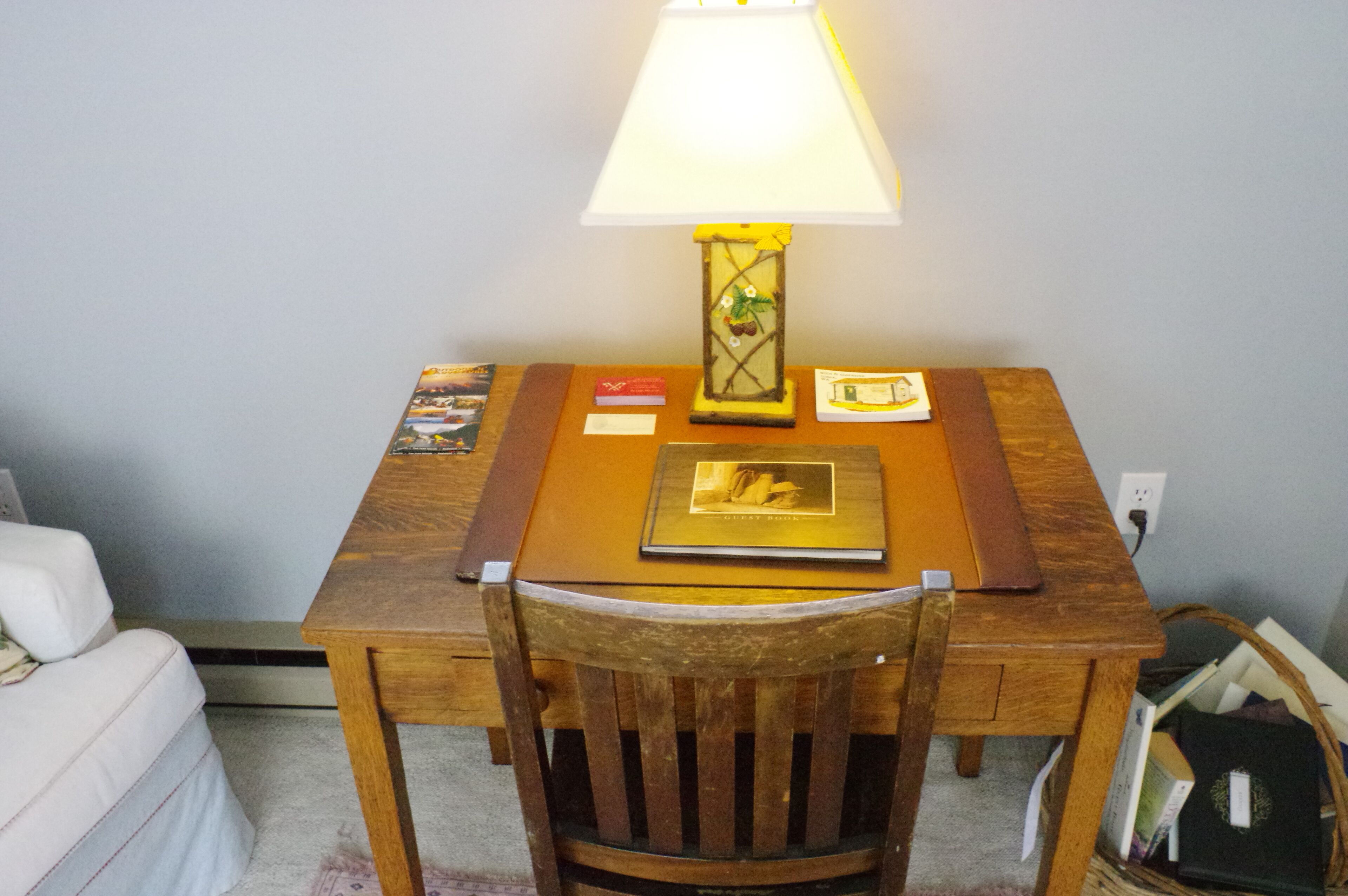 A wooden desk with a lamp, a chair, and a basket of books.