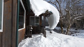 Une cabane en bois avec un porche enneigé et une rivière en arrière-plan.
