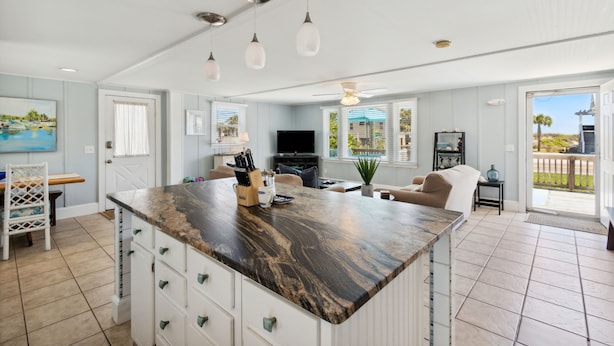 A spacious kitchen with a large island, white cabinetry, and a dining area with a chair and table.