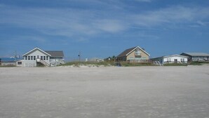 A beachside property with a sandy foreground, a few houses, and a clear sky.