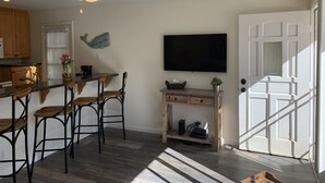 A modern kitchen with a dining area, wooden chairs, a ceiling fan, a flat-screen TV, and a door with a window. - 2 BR on Jersey Ct Just Steps to The Beach (San Diego)