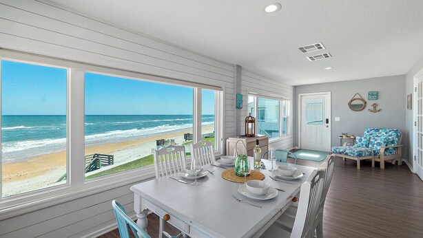 A dining area with a view of the beach, white furniture, and a table set for four.