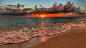 A beach with waves gently lapping at the shore and a sunset in the background.