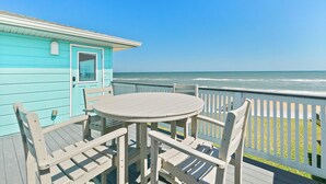 A turquoise wooden deck with a round table and chairs, overlooking the ocean.