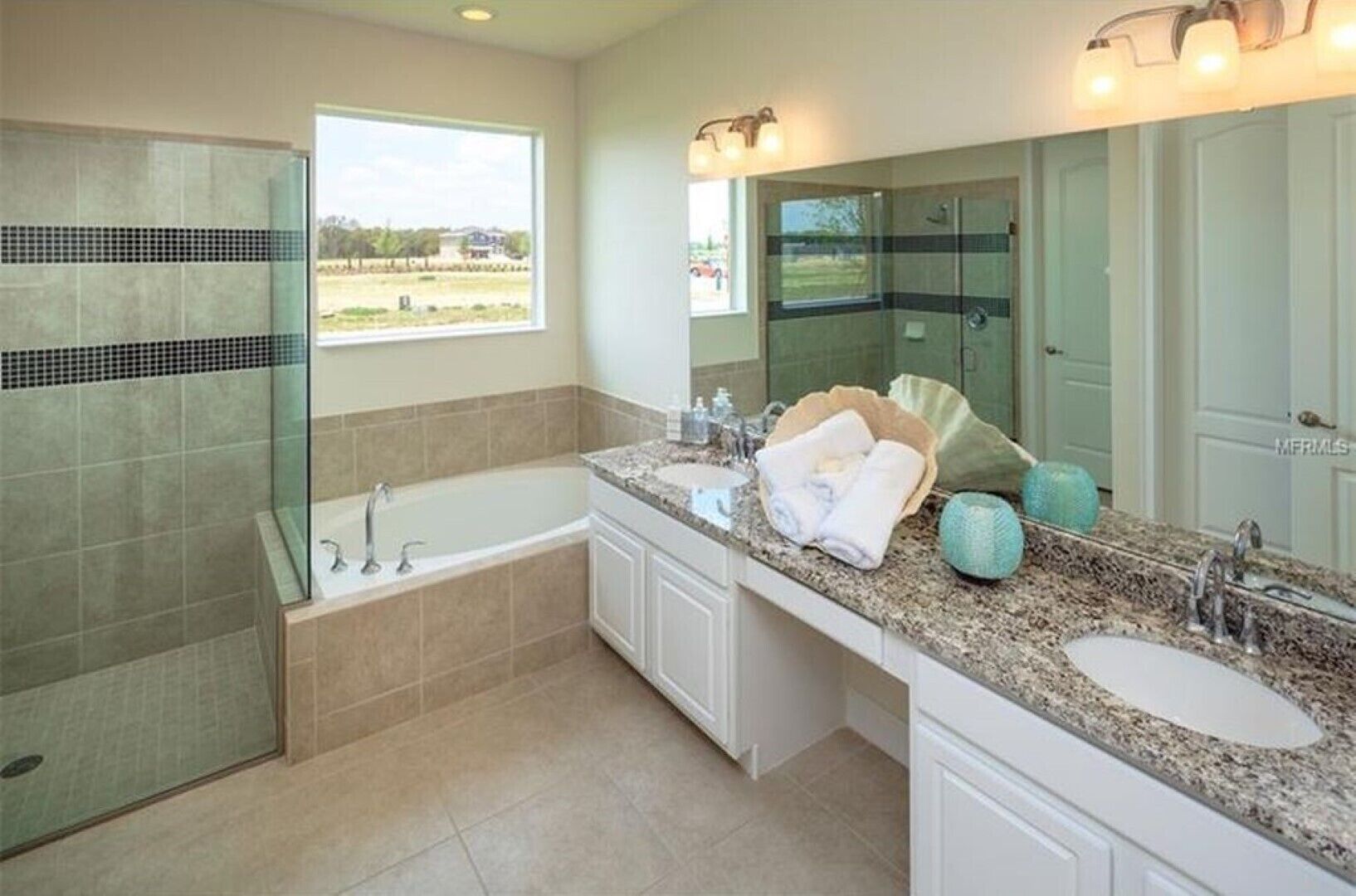 Un bagno moderno con doccia a vetro, vasca freestanding, un ampio lavabo con piano in granito e uno specchio grande.