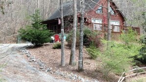 Eine rustikale Holzhütte mit Veranda, umgeben von Bäumen und einem Kiesweg.