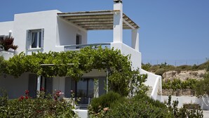 Un edificio moderno blanco con balcón, rodeado de exuberante follaje y flores.