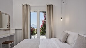 Un dormitorio con una cama grande, vista a flores rosadas por la ventana y un tocador blanco.