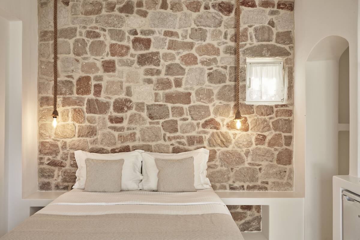 A bedroom with a stone wall, a bed with white bedding, and a small window with curtains.