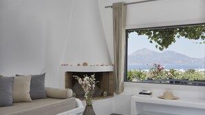 Una sala de estar moderna con sofá, chimenea, mesa de centro y un ventanal con vistas a montañas y al mar.