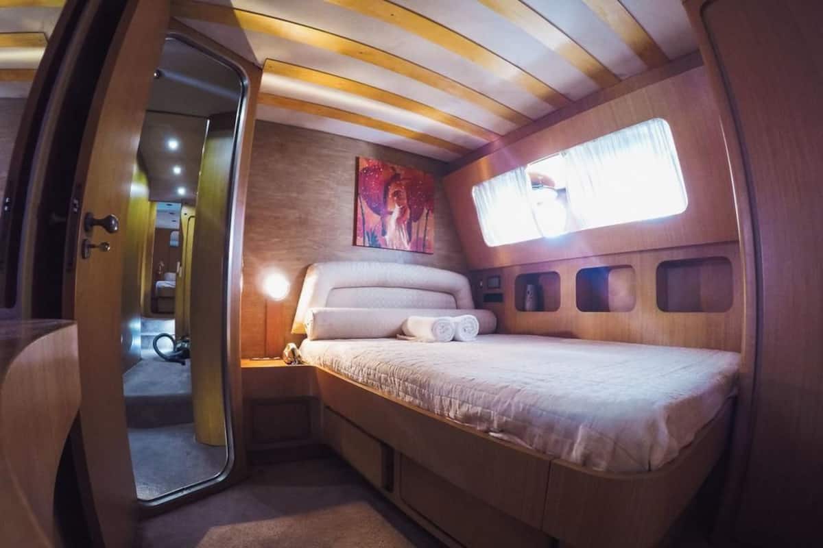 A compact bedroom with a bed, a painting, a window, and a door leading to another room.