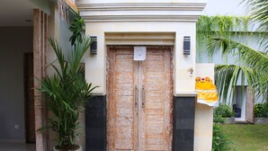 A wooden double door with a sign above it, flanked by potted plants and a small step leading up to the door. - Rusty Seminyak (Seminyak)