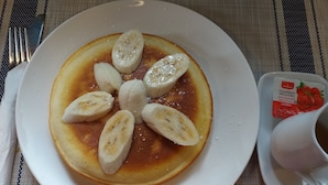 Ein Teller mit Pfannkuchen, belegt mit Bananenscheiben und einer kleinen Portion Erdbeerkonfitüre.