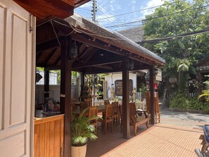 A wooden outdoor seating area with tables and chairs, a potted plant, and a signboard. - Xayana Home (Luang Prabang)