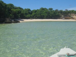 A beach with clear water, a sandy shore, and dense greenery in the background. - Emeraude lodge (Antsiranana)
