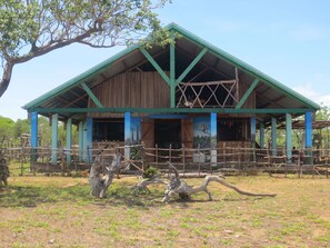 Un granero rústico con techo verde y estructura de madera, rodeado por un área cercada con árboles y cielo despejado.