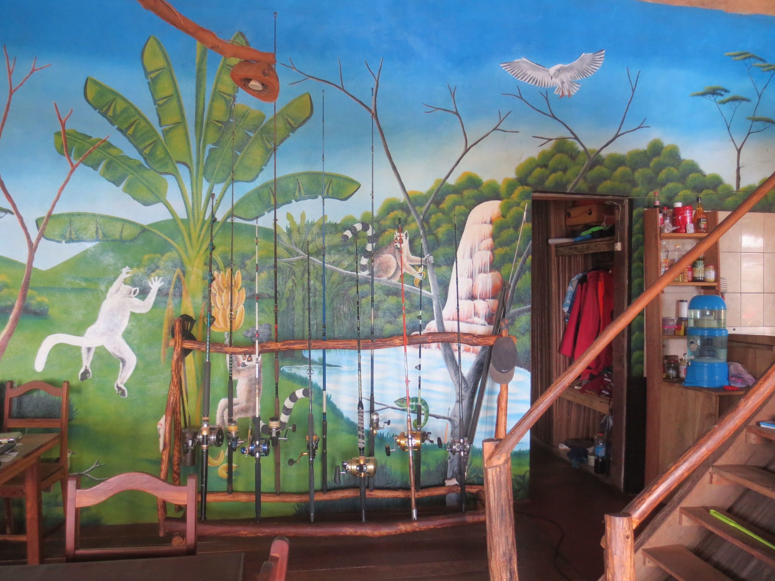 A room with a mural depicting a jungle scene, a wooden staircase, and a small table with chairs.