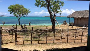 A fenced area with a thatched-roof hut, a tree, and a view of the sea. - Emeraude lodge (Antsiranana)