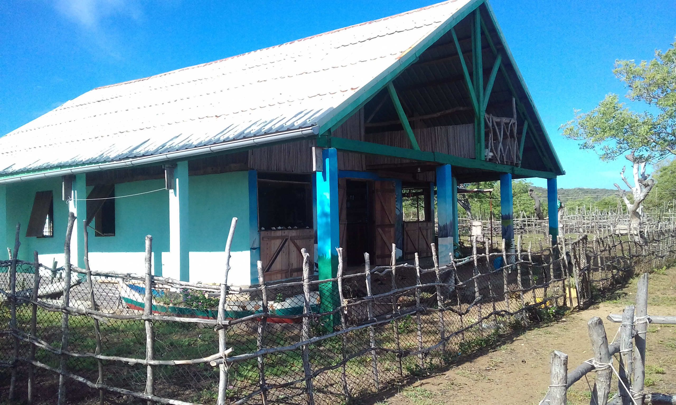 A rustic building with a metal roof and wooden walls, surrounded by a wire fence.