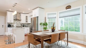 Une cuisine moderne avec des meubles blancs, des appareils en acier inoxydable et un coin repas avec une table dressée pour quatre personnes.