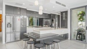 A modern kitchen with a central island, stainless steel appliances, and a glass door leading to a balcony. - Belle Escapes Tranquil Waters Luxury Home Palm Cove (Palm Cove)
