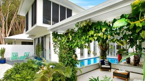 A modern house with a covered patio, a pool, and various plants. - Belle Escapes Tranquil Waters Luxury Home Palm Cove (Palm Cove)