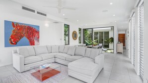 A modern living room with a large sectional sofa, a glass coffee table, and a vibrant zebra painting on the wall. - Belle Escapes Tranquil Waters Luxury Home Palm Cove (Palm Cove)