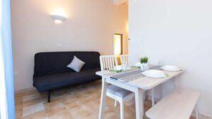 Ein kleiner Wohnraum mit einem dunklen Sofa, einem weißen Esstisch für zwei Personen und einer Bank.