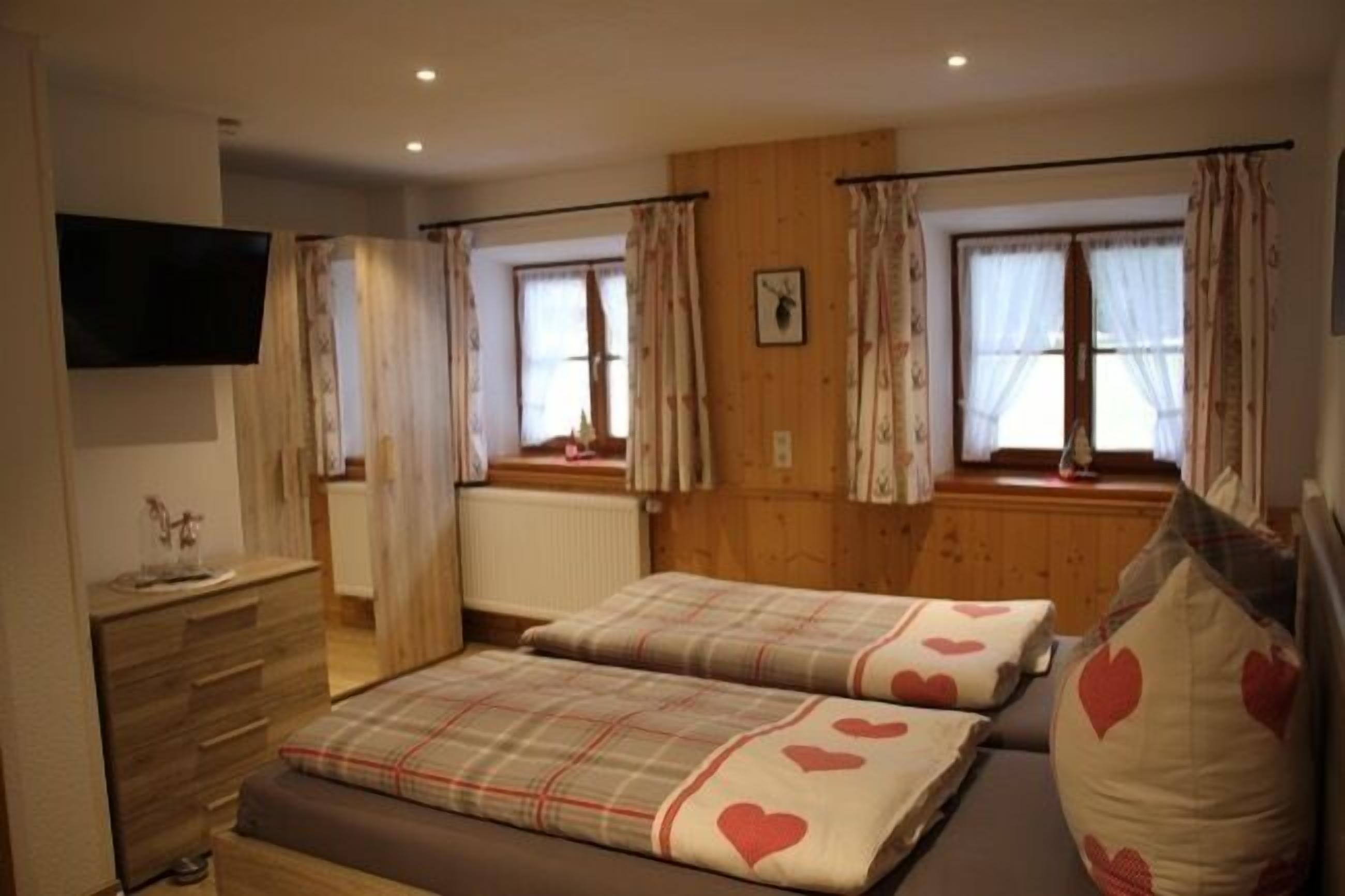 Une chambre avec deux lits, un lambris en bois, une commode, un téléviseur à écran plat et des fenêtres avec des rideaux.