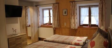A bedroom with two beds, wooden paneling, a dresser, a flat-screen TV, and windows with curtains.