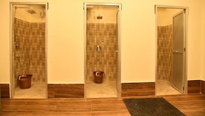 Une salle de bain d’hôtel avec trois cabines de douche en verre, chacune dotée d’un mur carrelé de carreaux bruns et d’un robinet en métal.