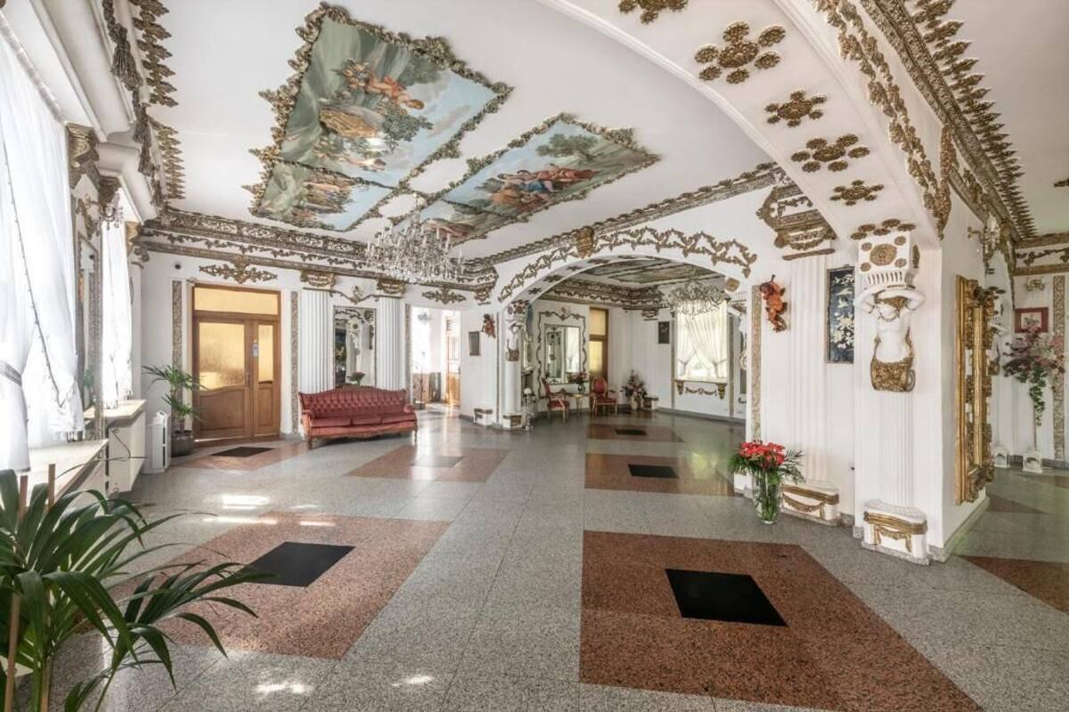 Un vaste hall d’entrée orné de motifs décoratifs au plafond, avec un canapé rouge et un lustre.