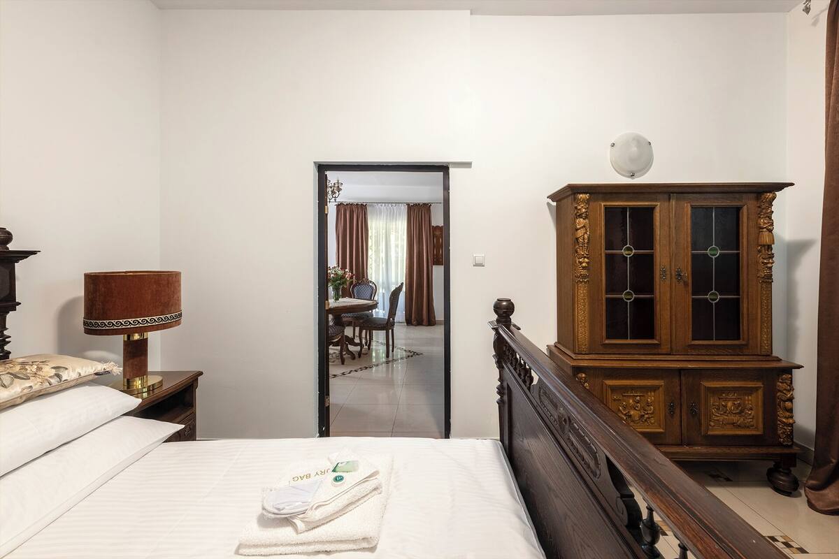 Une chambre d’hôtel avec un lit, une armoire en bois aux portes vitrées, une lampe et un miroir qui reflète un coin repas.