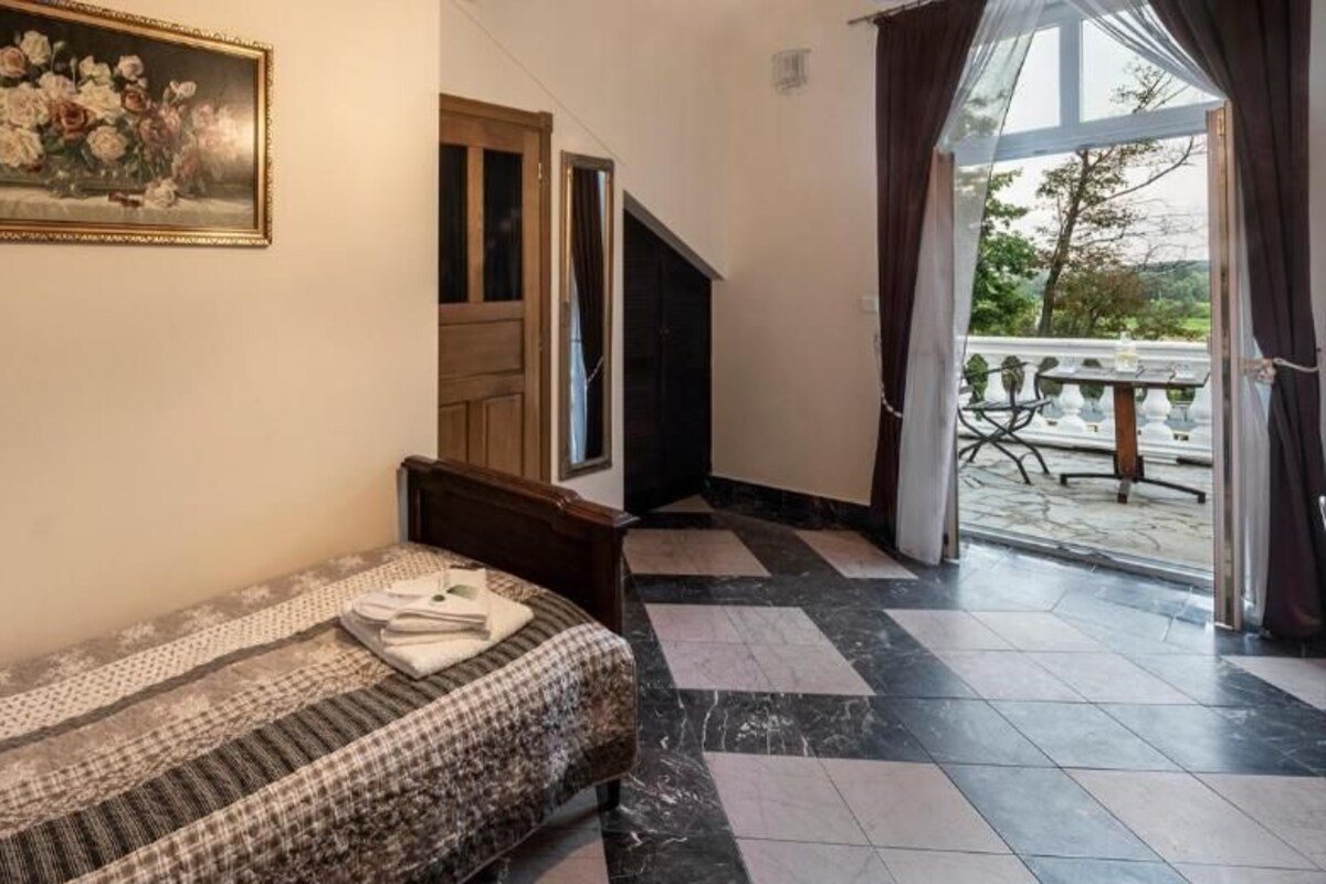 Ein Schlafzimmer mit Bett, einem Gemälde, einem Fenster und Blick ins Freie.