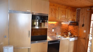 Una cocina compacta con armarios de madera, refrigerador de acero inoxidable, lavavajillas y salpicadero de ladrillo.